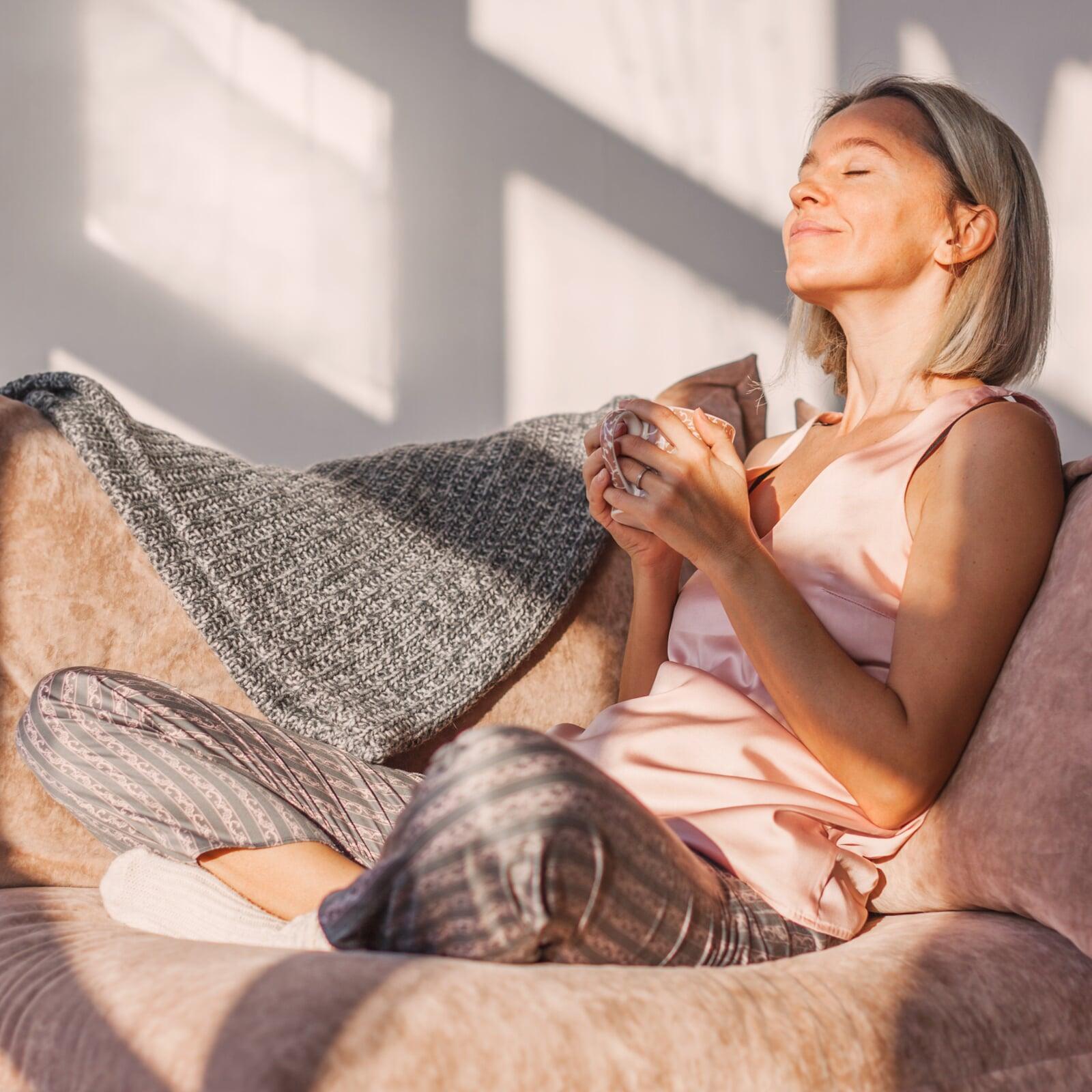 Entspannte Frau mit Tee auf einer Couch im Sonnenlicht.