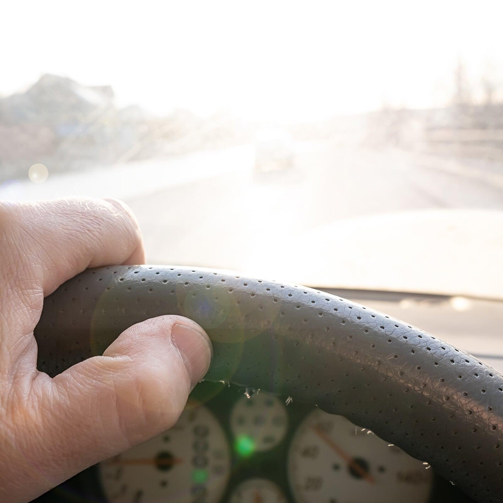Hand auf Lenkrad im Auto in Nahaufnahme mit starker Blendung von vorne.