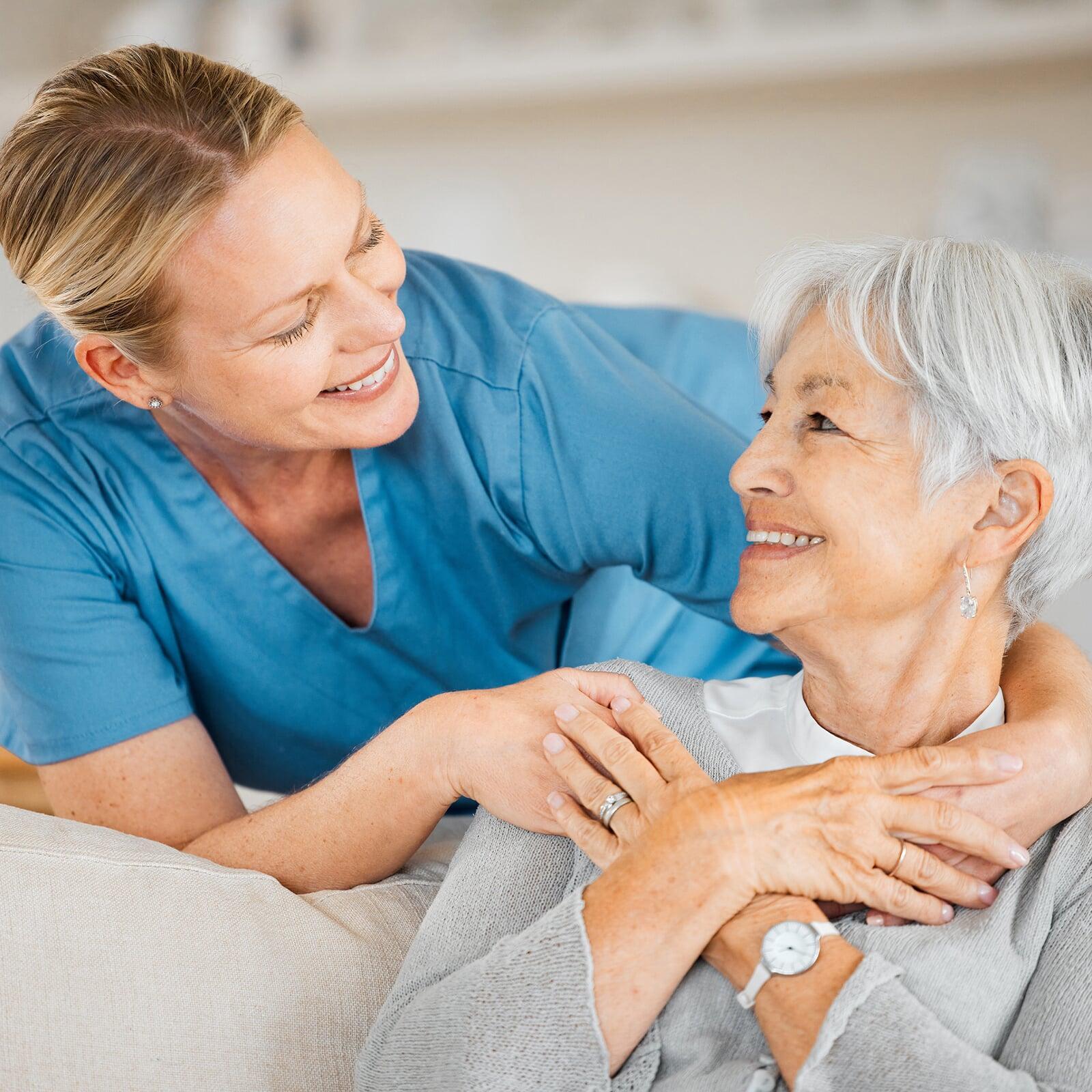 OP-Schwester beruhigt nervöse Dame durch Umarmung, beide lächeln sich an.